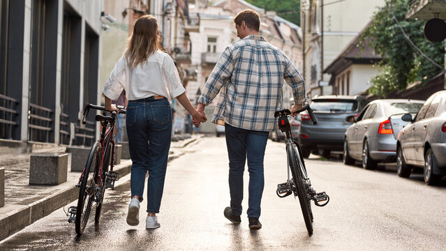 Back view of couple hold hands and walk with bikes