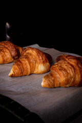 Fresh croissant on dark mood background and copy space for your product. Freshly backed french croissants shiny in the rays of the morning sun close up. Viennoiserie in France.
