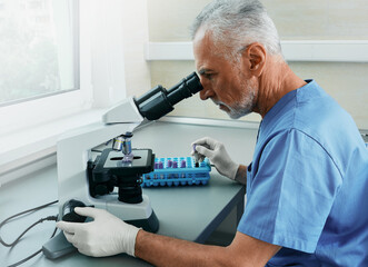 Professional male scientist looking in microscope while working on medical blood research in...