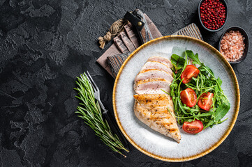 Sliced chicken breast fillet steak with green salad in a plate. Black background. Top view. Copy...