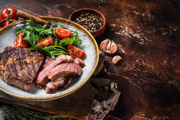 BBQ Grilled rib eye steak, fried rib-eye beef meat on a plate with green salad. Dark background. top view. Copy space