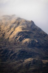 Vertical shot of mountains in early morning fog and clouds in the Scottish Highlands - obrazy, fototapety, plakaty