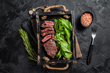 BBQ roasted flank steak in wooden tray with vegetable salad. Black background. Top view