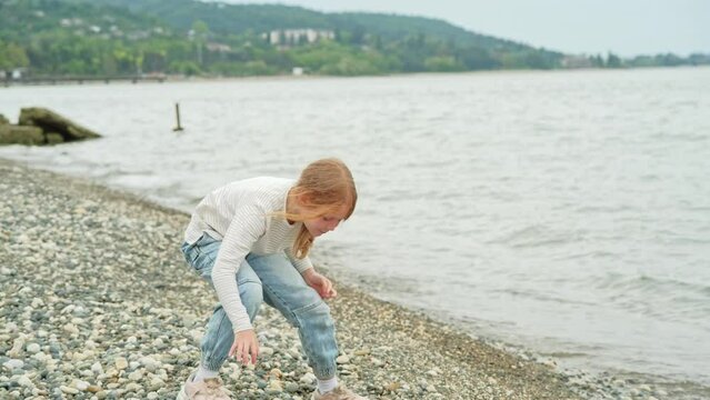 a little girl in jeans walks along the seashore
