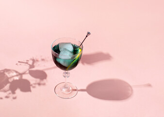 Blue drink, ice cubes and cocktail stick in vintage style tall glass, flower's silhouette on pastel pink background. Creative summer holidays inspired layout.