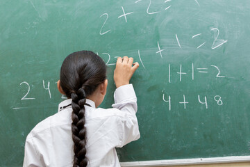 Back view of Indian schoolgirl write on chalkboard or blackboard in classroom, Education concept.