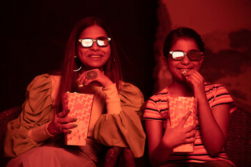 Happy young indian woman and girl child wearing 3d glasses eating popcorn and laughing while...