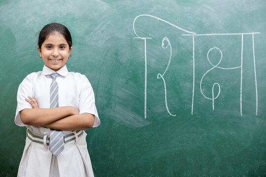Happy Indian school girl child standing over green chalkboard background with shiksha word writing in hindi.