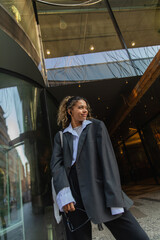 smiling african american woman in wireless earphone holding sunglasses on urban street in prague.