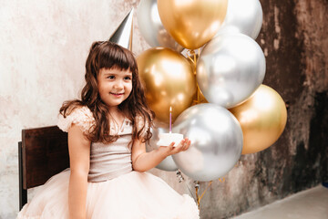 A happy little girl makes a wish and blows out the candles on the cake. balloons. Space for text....
