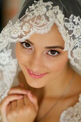 Beautiful girl bride in white dress and veil. Portrait of a woman before the wedding in the room.