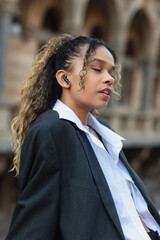 Fototapeta premium african american woman with closed eyes listening music in wireless earphone on urban street of prague.