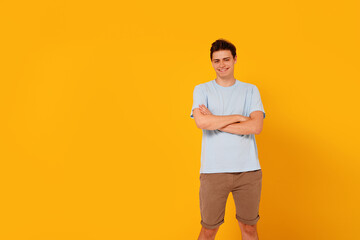 Fototapeta na wymiar Fashionable young student boy standing on the yellow studio background, looking and smiling at the camera.