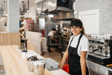 Beautiful and happy young female worker working in a bakery or fast food restaurant and using...