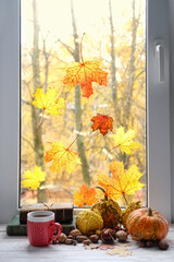autumn background. Tea cup, pumpkins, nuts, books and autumn leaves on window sill. symbol of fall season. home cozy composition for Halloween, Thanksgiving holidays.