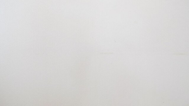 a hand paints a white wall with a construction paint roller