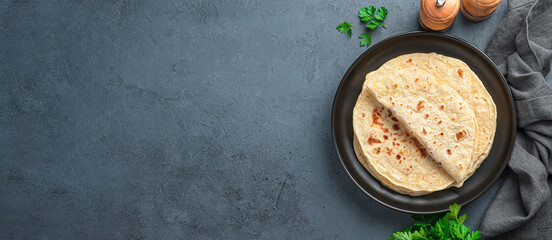 Fototapeta Chapati, traditional tortillas with fresh parsley on a graphite background. Indian flatbreads. Top view, copy space obraz