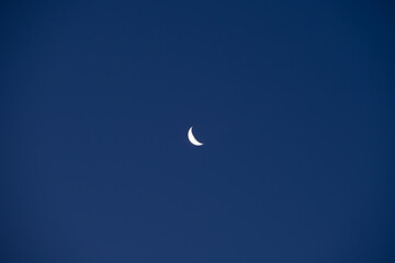 A crescent moon in a bright blue sky. Copy space