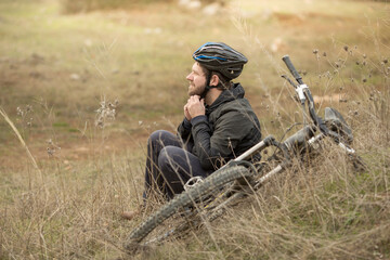 .a young man sits next to a mountain bike and fastens a helmet on his head