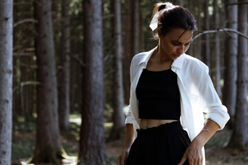 A young student walks in the woods. Looking down. Not looking at the camera. The sun is setting in the forest. The girl in the white shirt. The portrait is waist high. Blogger traveler