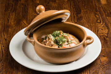 pot with stewed potatoes with meat and mushrooms in white gravy on a wooden board restaurant serving dishes food lunch dinner