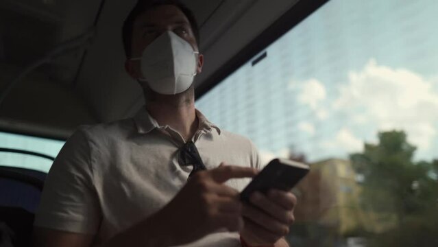 Commuting during pandemic. Public transportation curfew. Using cell phone while commuting to work on public transportation bus while wearing mask to prevent corona virus. Social distancing on bus 