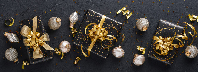 Merry Cristmas. Holiday gift box or present with ribbon, golden confetti and gold baubles on black background. Magic christmas greeting card. Christmas Decoration. Mock up. Top view. Banner.