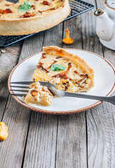 Homemade quiche or tart with chanterelles on rustic wooden background.