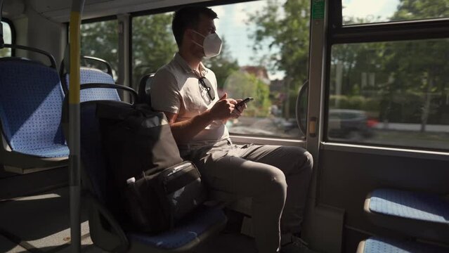 Passenger in ffp2 mask is on bus in Munich, browsing the Internet on mobile phone. Coronovirus regulations in Germany. Personal hygiene. Man on public transport using mobile app. Travel safely 