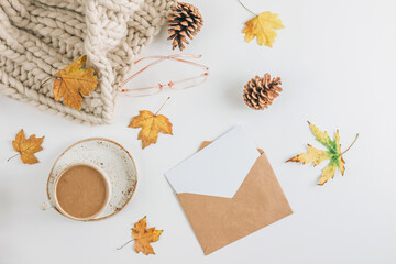 White and beige Autumn flat lay composition. Cup of coffee, scarf, glasses, cones, envelope and autumn leaves on white background.