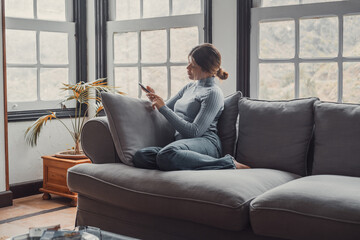Young beautiful woman sitting on the sofa at home chatting and surfing the net. Female person...