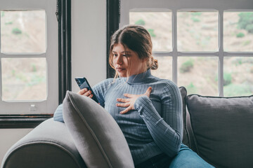 Portrait of impressed pretty female person staring phone bad fake news isolated on sofa at home. Young woman looking and reacting to something..
