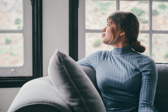 One Cute And Beautiful Young Girl Looking Outdoors At The Window From The Sofa Relaxing And Resting. Thoughtful Woman Pensive And Thinking Sitting On The Couch.