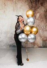 A girl with balloons is laughing against the background of a decorative wall. A beautiful happy woman on the birthday of a New Year's holiday party having fun holding a glass of champagne