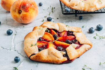 Galette, rustic sweet open pie with peach and blueberry on gray marble background.