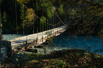 Beautiful, atmospheric shot of a wooden bridge over a mountain river for cars and people on a sunny autumn day. Impressive landscape of mountains, wooden bridge over the river