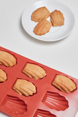 Cropped close-up shot of freshly baked cookies in a red silicone mold, cookies on a white plate on a white table. Top view.