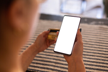 Close up young woman holding bank credit card and modern tech device with mock up white screen in hands, enjoying purchasing goods in internet store using mobile phone application, online shopping