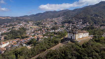 Fototapeta na wymiar Visão panoramica de igreja em cidade histórica de Ouro Preto Minas Gerais em meio a montanhas e céu nublado construções e casas antigas ao fundo