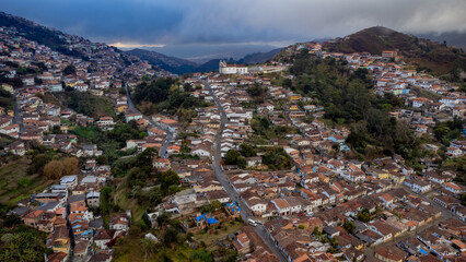 Visão aérea de cidade histórica em minas gerais com ladeiras e igrejas ao fundo casas e construções antigas céu nublado em meio a montanhas