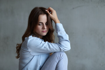 Young Woman in Casual Attire Sitting Against a Gray Background in a Thoughtful Pose