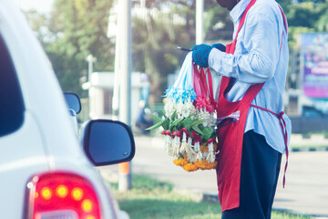 The man is selling flowers to motorists at a traffic lights junction with looking smartphone
