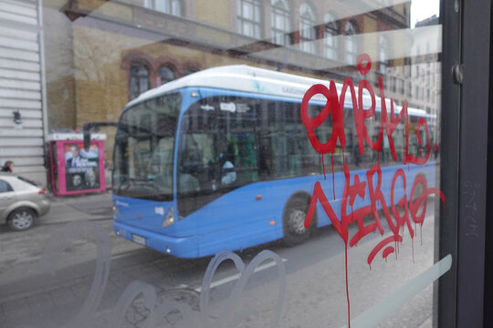 Graffiti on the window of the bus stop and a bus passing