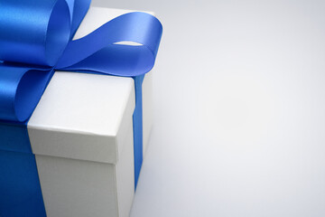 close-up silver gift box with blue satin bow ribbon on grey background