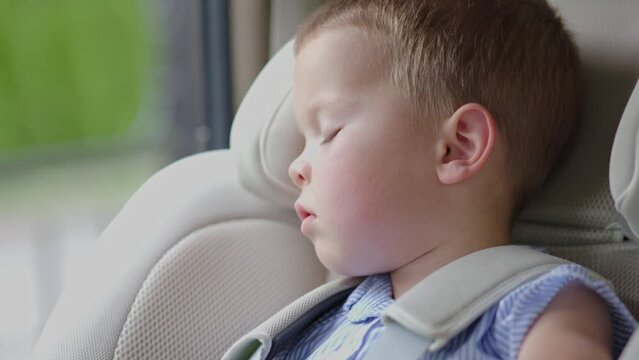 sweat dreams baby sleeping in car seat inside vehicle, face boy child napping. young passenger taking nap in back of vehicle in sunny summer day. tired preschooler sleep inside auto. concept traveling