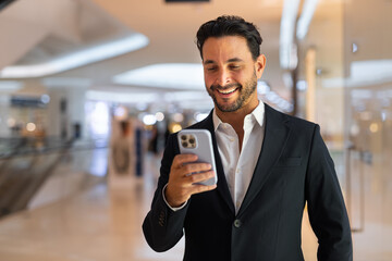 Portrait of happy handsome Hispanic businessman using mobile phone while smiling