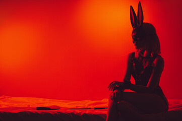 submissive sexy girl in underwear and a bunny mask sitting on the bed puts handcuffs on hands in...