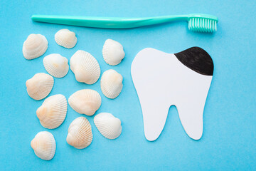 Tooth model with caries, toothbrush and seashells. Blue background. Flat lay. Top view. Benefits of minerals for dental hygiene. Oral care.