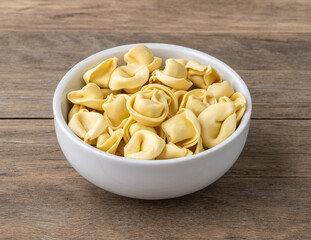 Uncooked cappelletti or tortellini on a bowl over wooden table