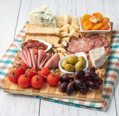 Appetizer board with cheese, nuts, fruits, toasts and charcuterie over wooden table